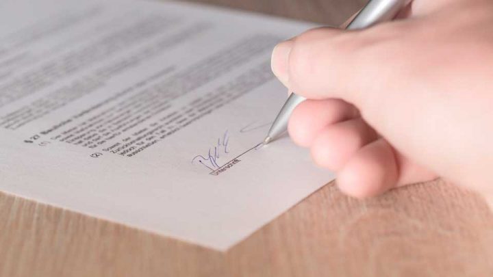 Imagem de mão assinando um contrato usando caneta prateada